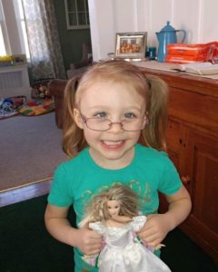 A little girl in glasses holds a doll