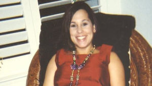 A woman wearing red sits in a chair and smiles