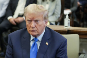 former President Donald Trump wears a blue suit and tie as he sits in a NY courtroom