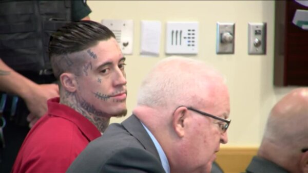 Man with tattoos on his face sits in court next to his attorney.