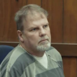Bearded, grey-haired man in grey prison stripes.