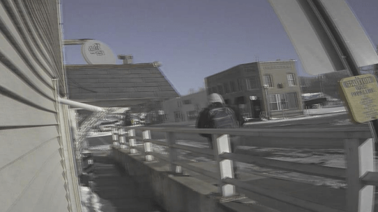 surveillance photo shows a person with a backpack walking along a road with a guard rail