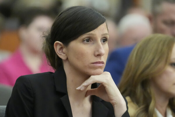 A concerned looking young woman looks on in court. She wears a black suit and a slick bun.