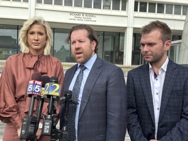 Three people stand behind microphones