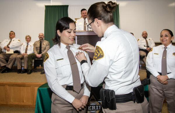 woman places pin on sheriff's uniform
