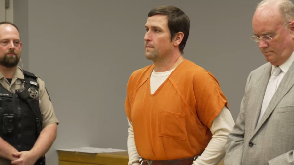 a man in jail uniform stands in court next to attorney