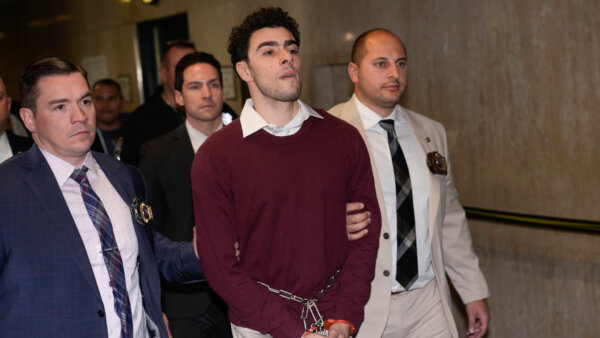 Young man in a maroon sweater is escorted down a hall.