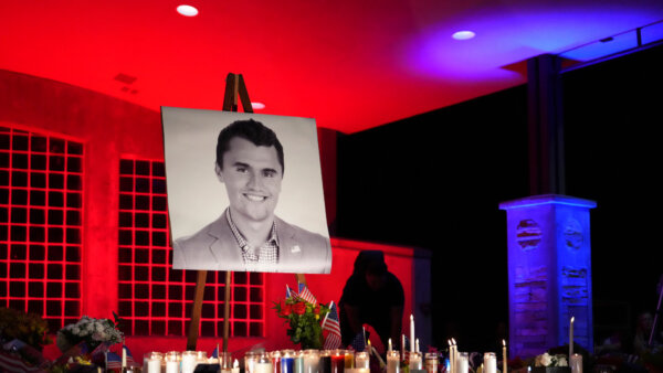 People place lit candles below a photo of Charlie Kirk