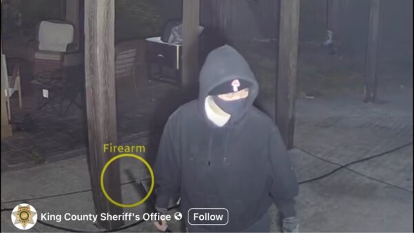person in hoodie and mask holds a gun