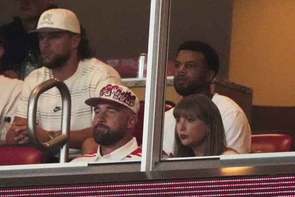 Travis Kelce and Taylor Swift sit at a sporting event.